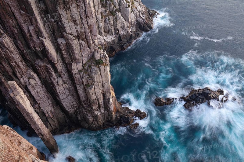 Long exposure at sunrise shows glowing dawn over the dramatic cliffs of Cape Hauy. Gentle waves hit the steep cliffs. Cape Hauy, Tasman Peninsula, Tasmania, Australia
