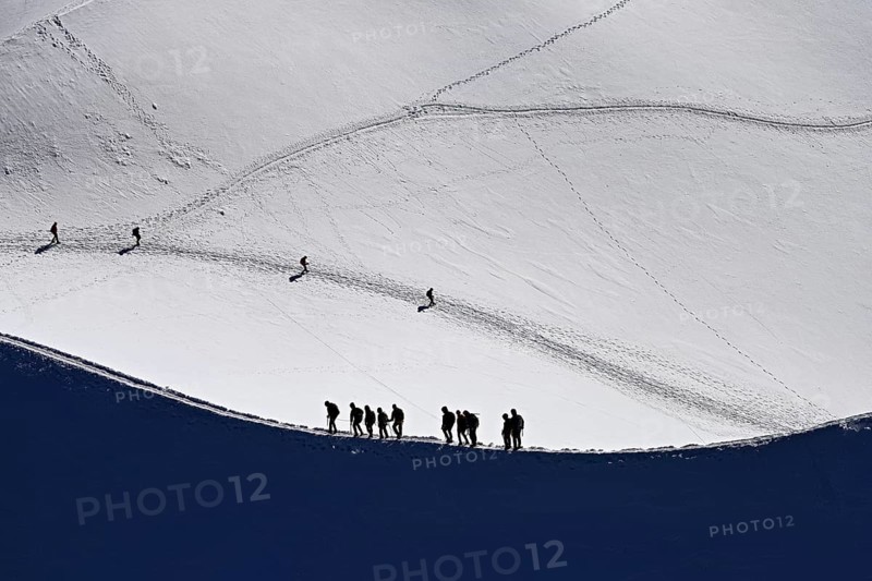 A group of mountaineers runs across a snow-covered mountain ridge, Aiguille du Midi, Chamonix-Mont-Blanc, Haute-Savoie, France