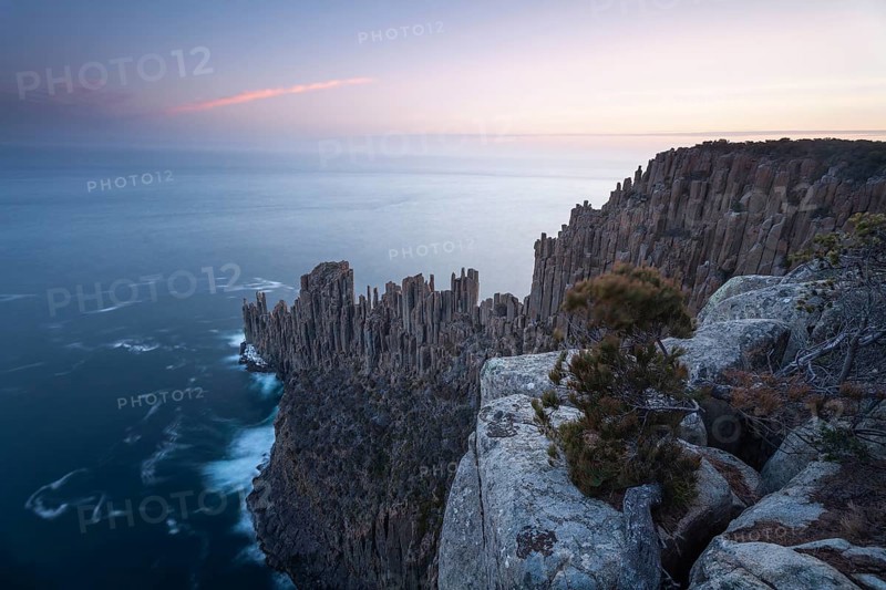 Long exposure shows sunset over the cliffs of Cape Raoul. Golden light hits the sea and colors the rocks warmly in the evening. Cape Raoul, Tasman Peninsula, Tasmania, Australia