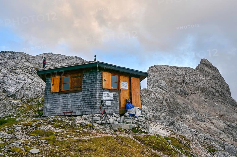 Two mountaineers relax at the Wildalmkirchl bivouac with the Wildalmkirchl summit in the background, Steinernes Meer, Berchtesgaden Alps, Austria