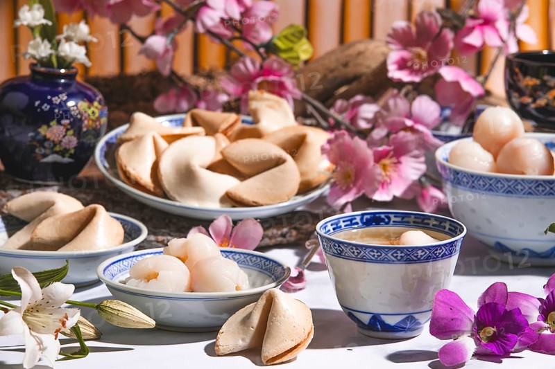 Lychee, lychee wine and fortune cookies in Asian tableware surrounded by blossoms