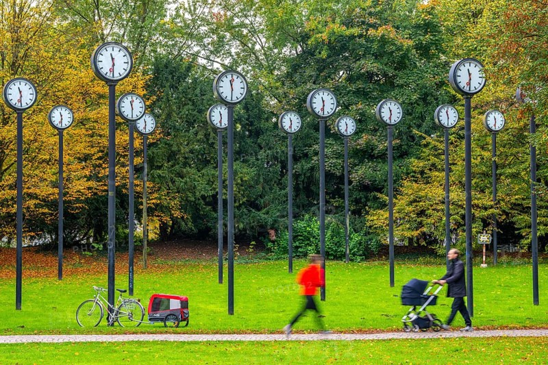 The art installation Zeitfeld in Volksgarten Park in Düsseldorf-Oberbilk, a total of 24 station clocks, on 6 meter high steel columns, have been running synchronously since 1987, jogger in the municipal park, artwork by Düsseldorf artist Klaus Rinke, symbol of time, time change, North Rhine-Westphalia, Germany