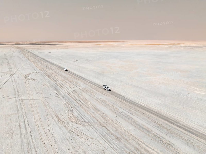Aerial view, two off-road cars driving on a salt pan, arid landscape, Botswana