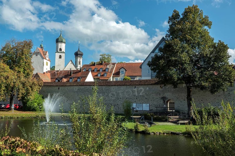 Trench pond with water fountain, city wall, church towers and water tower at the back, Isny, Allgäu, Baden-Württemberg, Germany