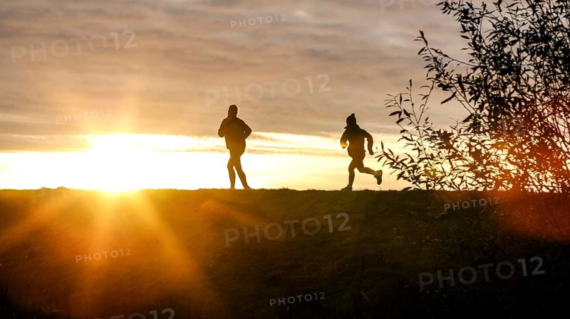 Woman and child walk across a dike on the island of Fehmarn at sunset, 13.10.2025, Fehmarn, Schleswig-Holstein, Germany