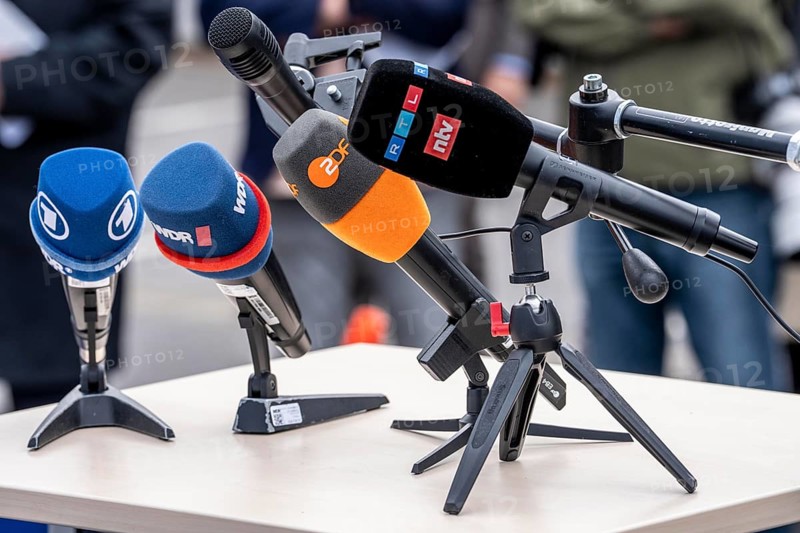 Microphones from various radio stations, television stations, standing on the table, at a press conference