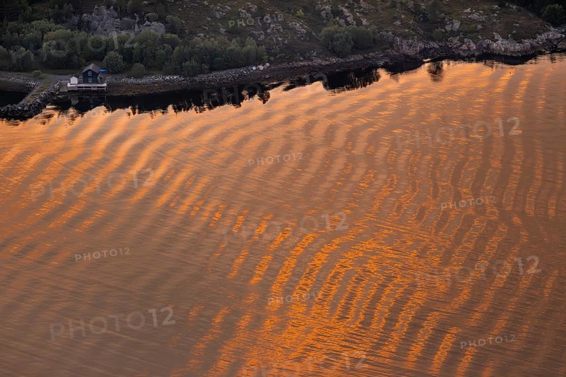 Warm sunlight reflects on gentle waves in a bay at sunset, forming a wave-like pattern, Otroya or Otrøya Island, Møre og Romsdal, Norway
