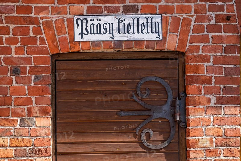 Wrought-iron fitting on wooden door and sign with Finnish inscription 'pääsy kielletty', no entry, brick wall, former paper mill for the production of groundwood pulp board, UNESCO World Heritage Site Verla Factory Village, Maailmanperintökohde Verlan puuhiomo ja pahvitehdas, Verla Rapids, Kymenlaakso, near Kouvola, Finland