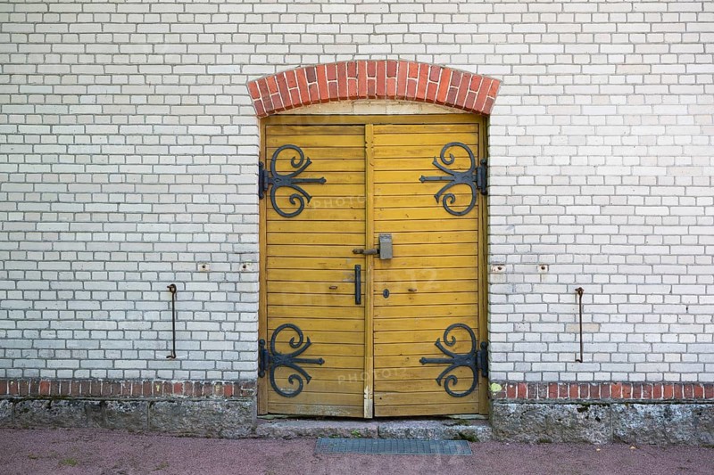 Yellow wooden door with wrought-iron fittings, white brick wall, former paper mill for the production of groundwood pulp board, UNESCO World Heritage Site Factory Village Verla, Maailmanperintökohde Verlan puuhiomo ja pahvitehdas, Verla Rapids, Kymenlaakso, near Kouvola, Finland