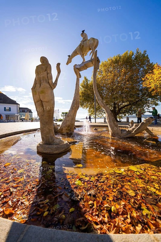 Artistic fountain with sculptures surrounded by autumn leaves and water, Überlingen, Lake Constance, Germany