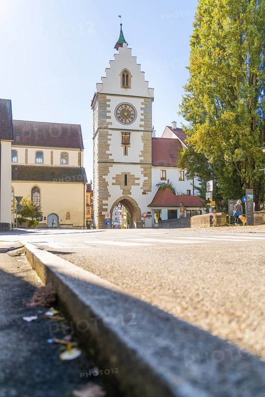 A historic tower with clock in a sunny street, surrounded by trees in autumn, Überlingen, Lake Constance, Germany