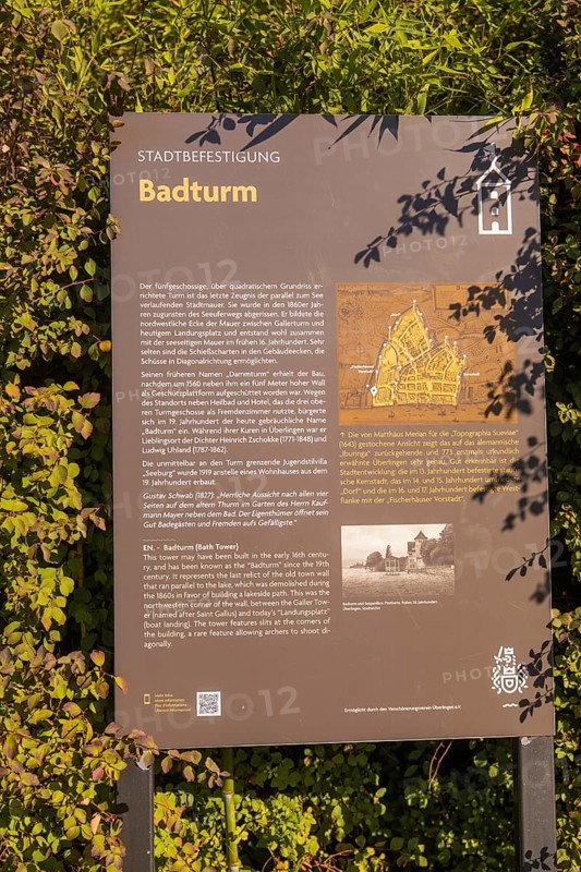 Information board about the Badturm with historical text and map, surrounded by green plants, Überlingen, Lake Constance, Germany