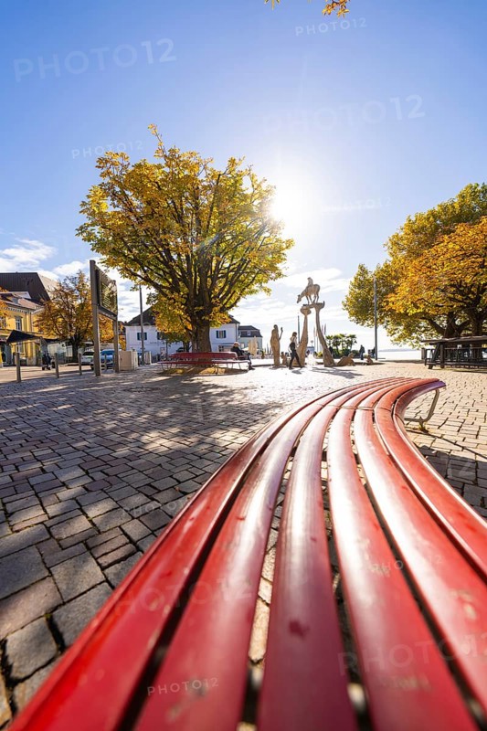 Red benches on a sunny town square surrounded by autumnal trees, Überlingen, Lake Constance, Germany