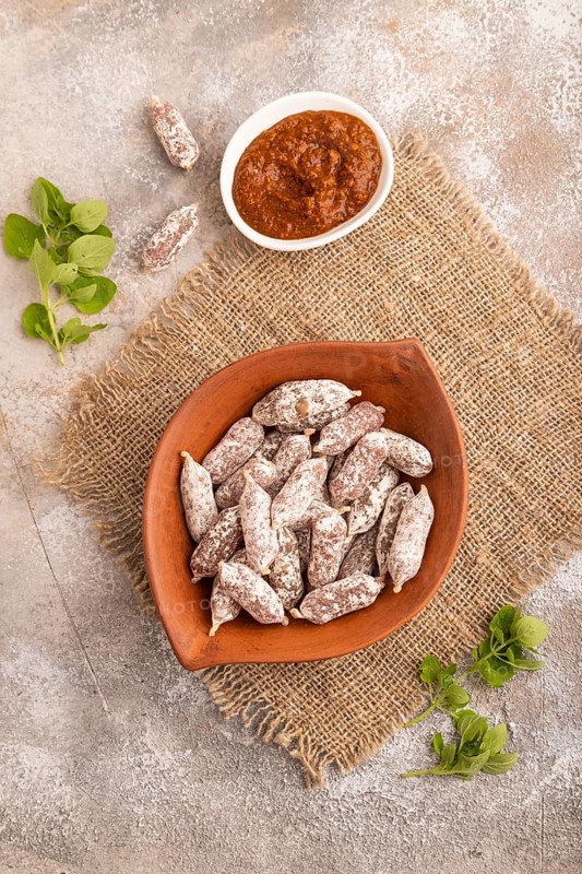 Small smoked Chicken sausages in clay bowl on brown concrete background and linen textile. top view, flat lay, close up