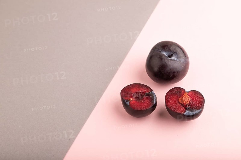 Purple Plum Cut in half on pink and gray pastel paper background. Side view, copy space. healthy food, vegetable, minimalism