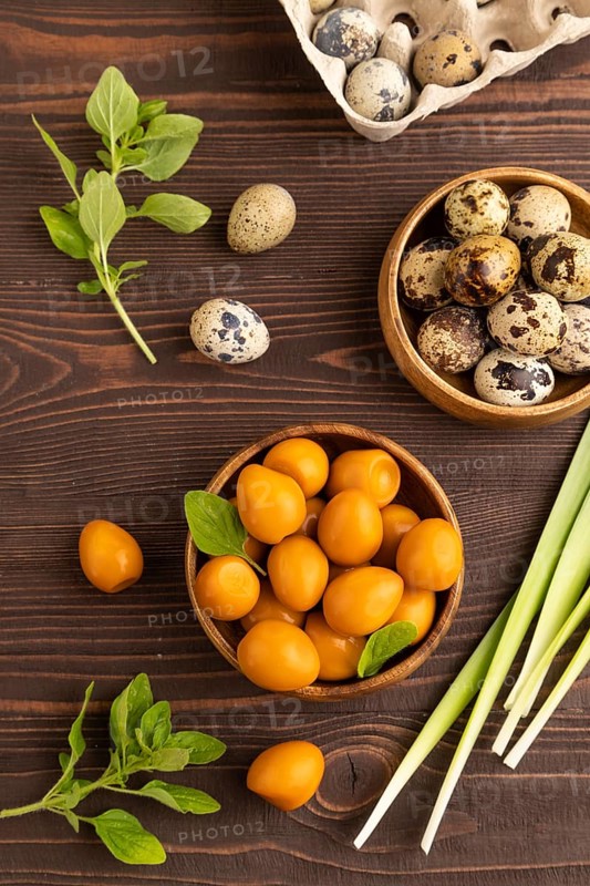 Pile of Smoked Quail eggs in bowl on a brown wooden background. top view, flat lay, close up