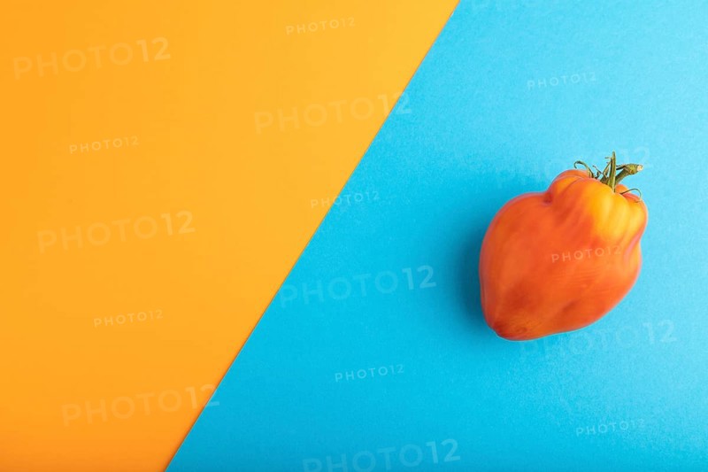 Red Heart Shape tomato on blue and orange pastel paper background. Top view, flat lay, copy space. healthy food, vegetable, minimalism