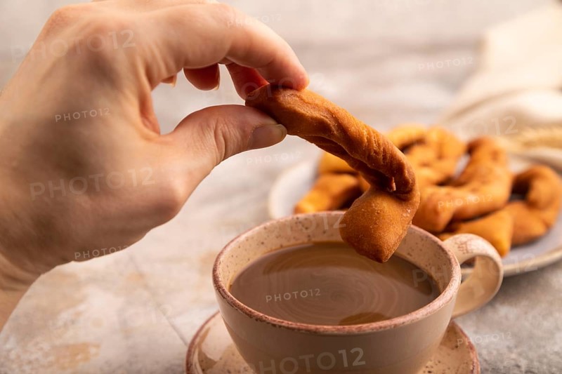 Crunchy biscuit Brushwood cookies with hand sprinkled with powdered sugar on brown concrete background and linen textile, cup of coffee, side view, selective focus