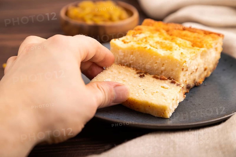 ?ottage cheese ?asserole, Curd cake, with dried apricots and raisins with hand on brown wooden background and linen textile, side view, close up, minimalism, selective focus