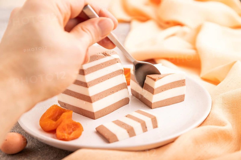 Cocoa and milk jelly with dried apricots with hand on brown concrete background and orange textile, side view, close up, selective focus, minimalism