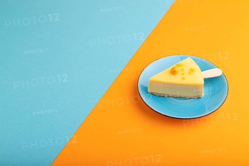 Yellow Cake pop with sprinkles on blue ceramic plate on blue and orange pastel paper background, side view, copy space, minimalism