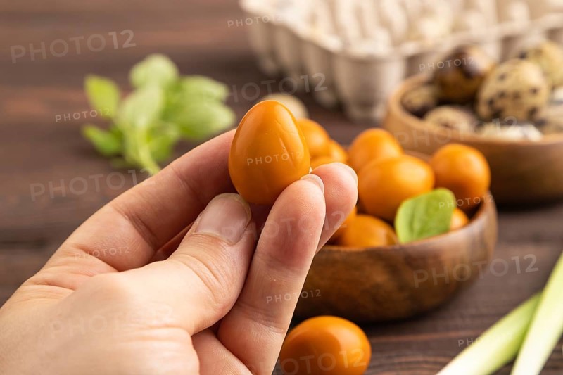 Pile of Smoked Quail eggs in bowl with hand on a brown wooden background. side view, close up, selective focus