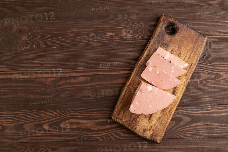 Mortadella sausage on wooden cutting board with pepper and herbs on brown wooden background. Top view, flat lay, copy space
