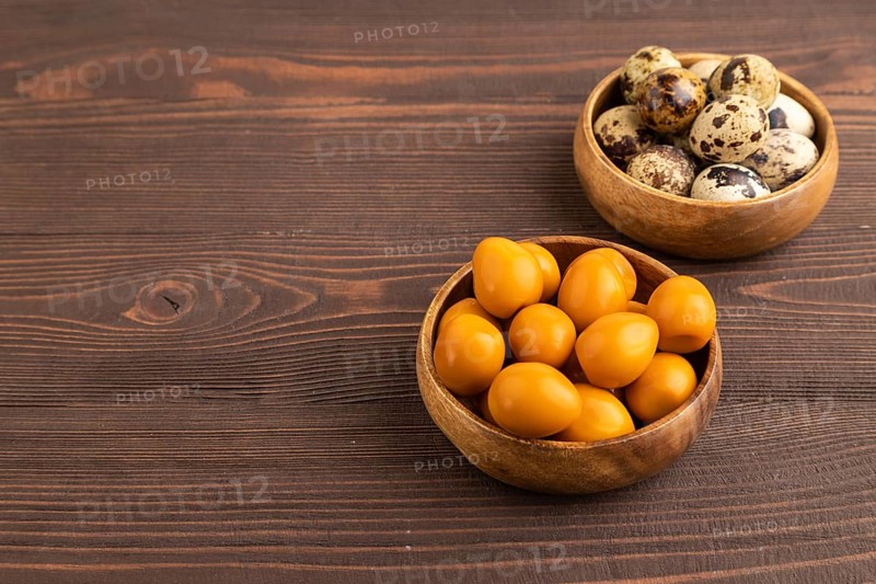 Pile of Smoked Quail eggs in bowl on a brown wooden background. side view, copy space