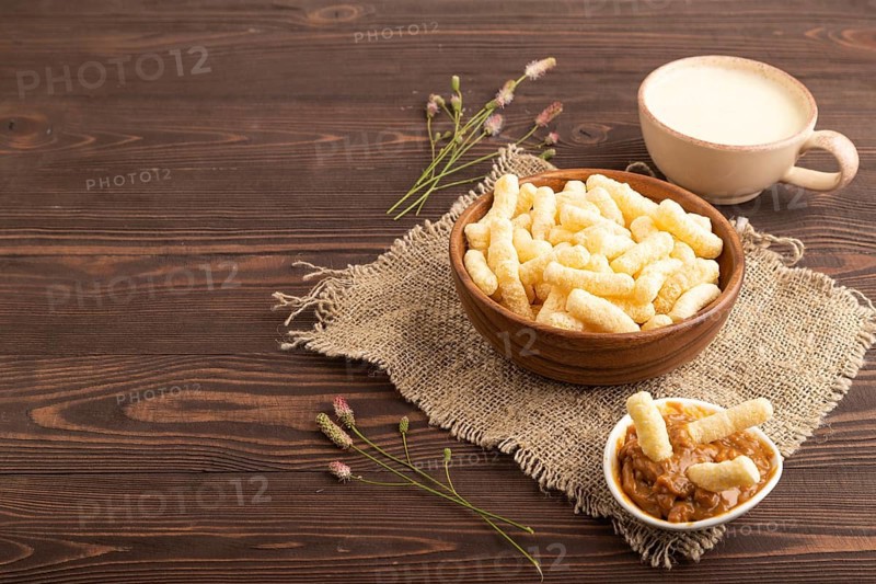 Corn flakes sticks with caramel in wooden bowl on brown wooden background and linen textile. Side view, copy space