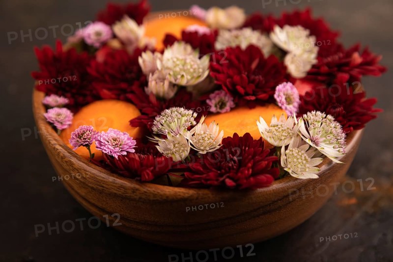 Wooden bowl with carrot slices and red Chrysanthemum flowers, Astrantia flowers, flower salad on black concrete background, side view, close up, minimalism, selective focus