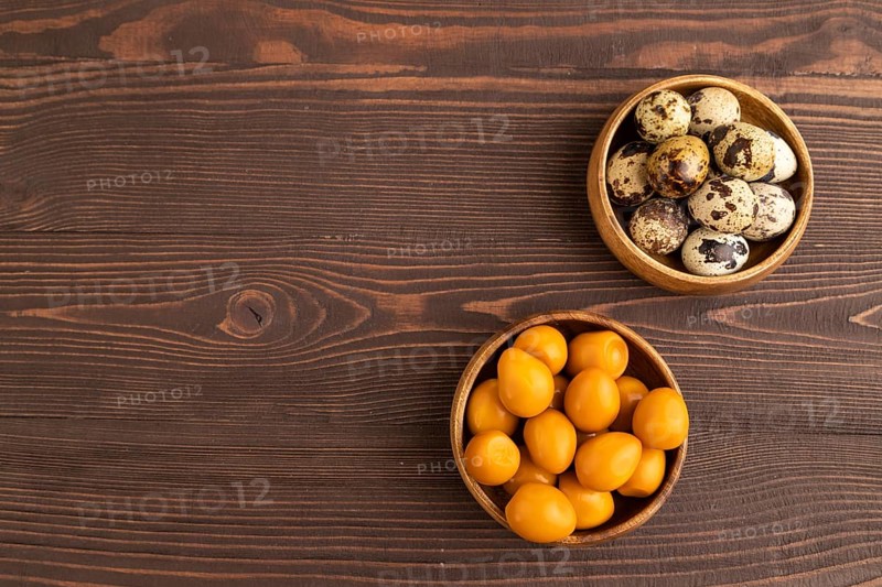 Pile of Smoked Quail eggs in bowl on a brown wooden background. top view, flat lay, copy space