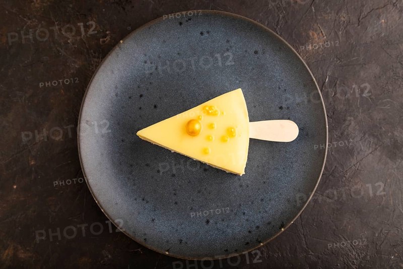 Yellow Cake pop with sprinkles on blue ceramic plate on black concrete background, top view, flat lay, close up, minimalism