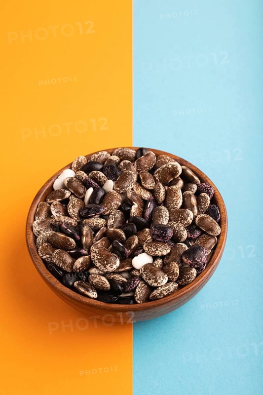 Wooden bowl with Kidney beans on blue and orange pastel paper background, side view, copy space, minimalism