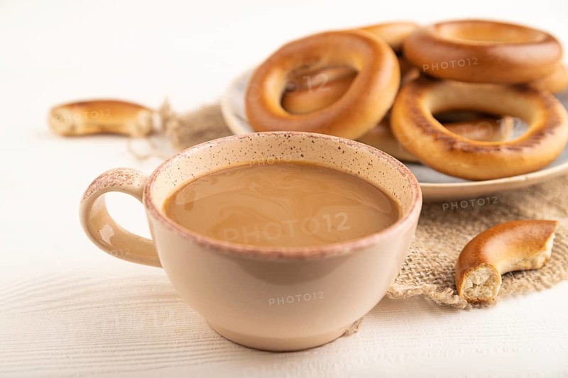 Homemade Ring Bagel with cup of coffee on white wooden background and linen textile. side view, close up, selective focus