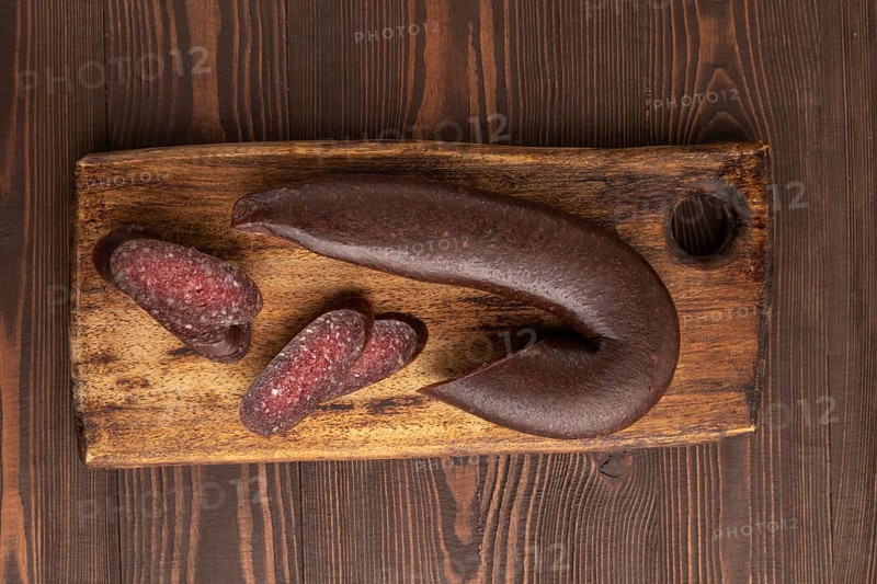 Sujuk sausage on wooden cutting board with pepper and herbs on brown wooden background. Top view, flat lay, copy space