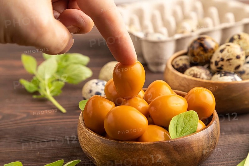 Pile of Smoked Quail eggs in bowl with hand on a brown wooden background. side view, close up, selective focus