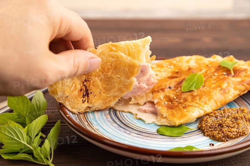 Fried homemade Khachapuri cake with cheese and meat, fried in pan with hand. Traditional Georgian cuisine on brown wooden background. Side view, close up, selective focus
