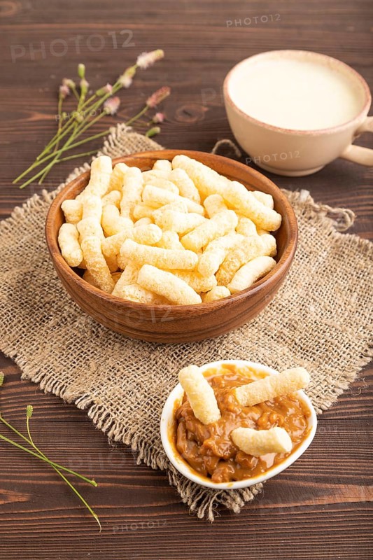 Corn flakes sticks with caramel in wooden bowl on brown wooden background and linen textile. Side view, close up