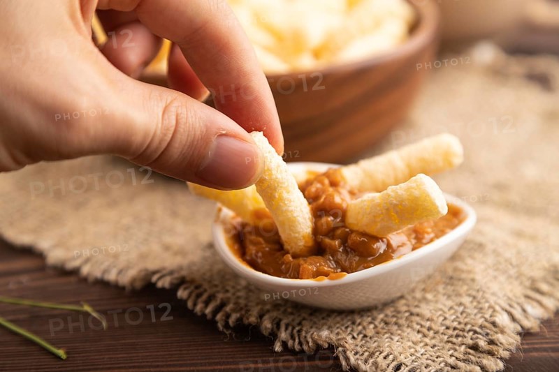 Corn flakes sticks with caramel in wooden bowl with hand on brown wooden background and linen textile. Side view, close up, selective focus