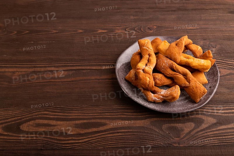Crunchy biscuit Brushwood cookies sprinkled with powdered sugar on brown wooden background, side view, copy space