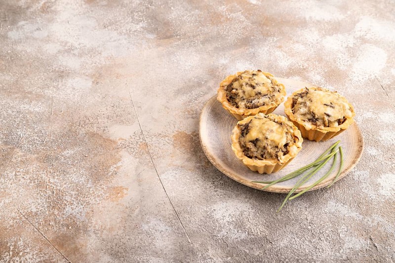 Tartlets with meat and cheese on brown concrete background. side view, copy space
