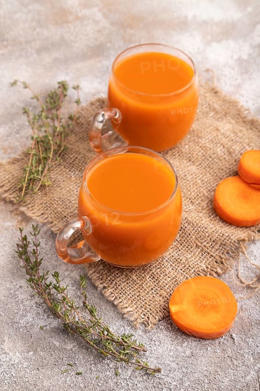 Two glasses with carrot juice, on brown concrete background and linen textile. Diet, healthy eating concept. side view, close up, minimalism