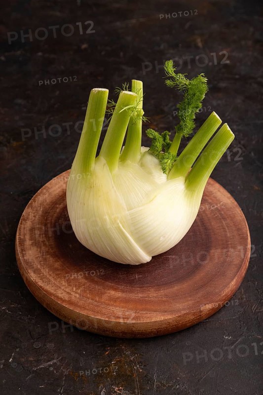 Fresh Fennel bulb on wooden cutting board on black concrete background, side view, copy space, minimalism