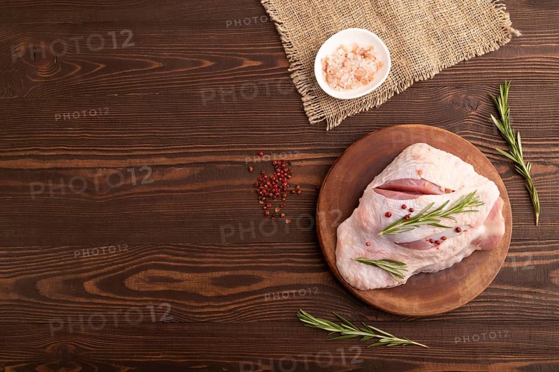 Raw Turkey Thigh with spices and rosemary on cutting board on brown wooden background and linen textile. top view, flat lay, copy space