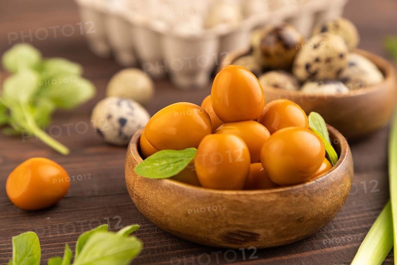 Pile of Smoked Quail eggs in bowl on a brown wooden background. side view, close up, selective focus