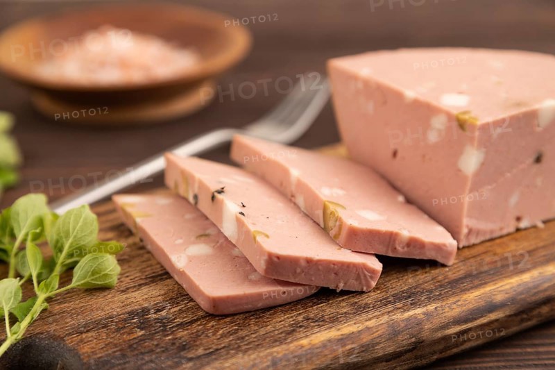 Mortadella sausage on wooden cutting board with pepper and herbs on brown wooden background. Side view, close up, selective focus