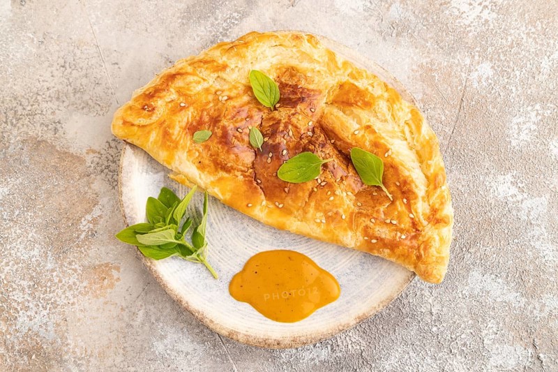 Fried homemade Khachapuri cake with cheese and meat, fried in pan. Traditional Georgian cuisine on brown concrete background. Top view, flat lay, close up
