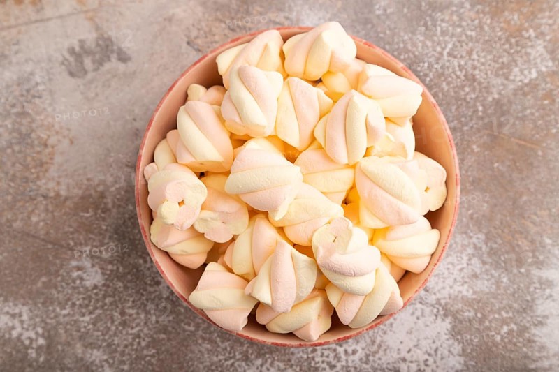 Orange and pink marshmallow in ceramic bowl on brown concrete background, top view, flat lay, copy space, minimalism