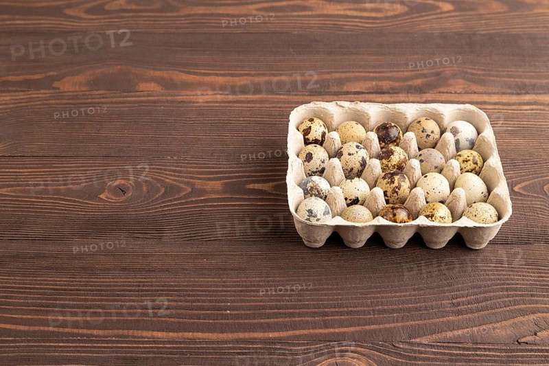 Pile of raw Quail eggs on brown wooden background. side view, flat lay, copy space