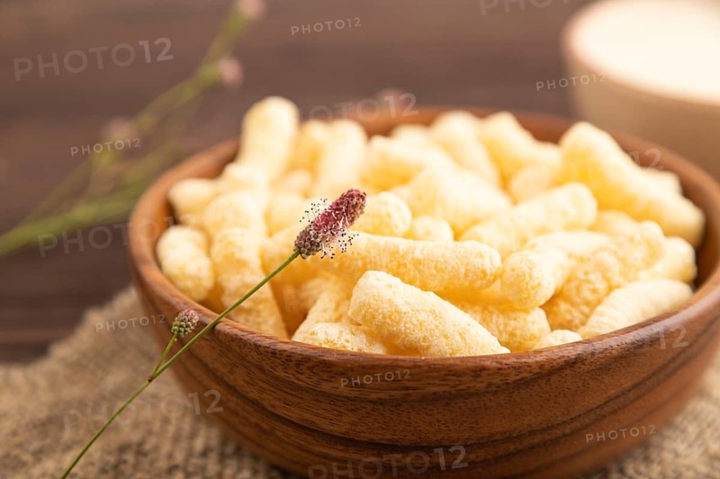 Corn flakes sticks with caramel in wooden bowl on brown wooden background and linen textile. Side view, close up, selective focus
